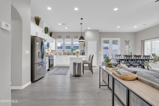 kitchen with a breakfast bar, hanging light fixtures, stainless steel appliances, white cabinets, and french doors