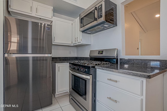 kitchen featuring white cabinets, appliances with stainless steel finishes, light tile patterned flooring, and dark stone countertops