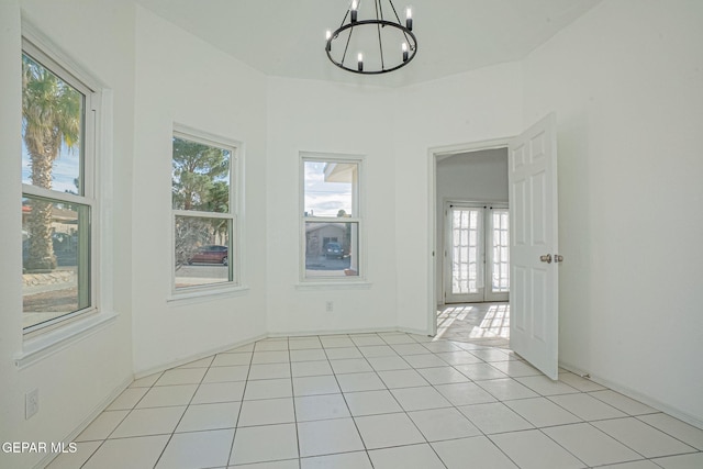 tiled empty room featuring a wealth of natural light and a notable chandelier