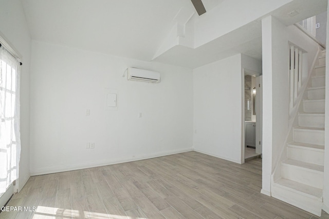 unfurnished room featuring light hardwood / wood-style floors, vaulted ceiling, and a wall mounted air conditioner