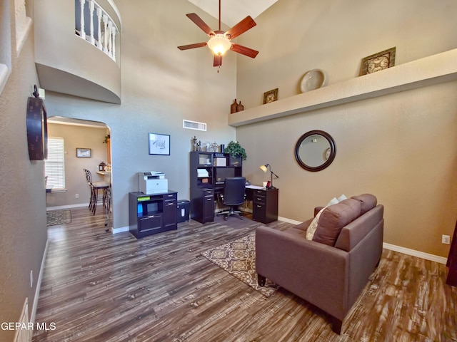 living room featuring ceiling fan, dark hardwood / wood-style floors, and a towering ceiling