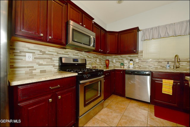 kitchen with sink, light tile patterned floors, stainless steel appliances, light stone counters, and decorative backsplash