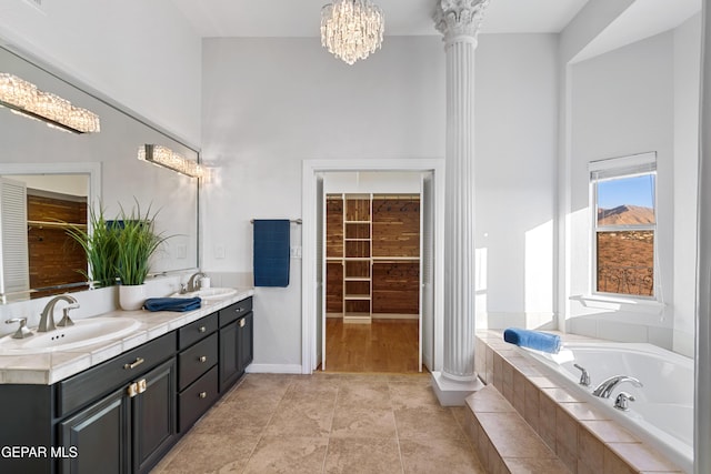 bathroom featuring vanity, tile patterned flooring, tiled tub, a chandelier, and decorative columns