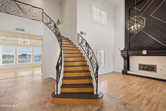 staircase featuring tile patterned flooring, a fireplace, a towering ceiling, and a chandelier