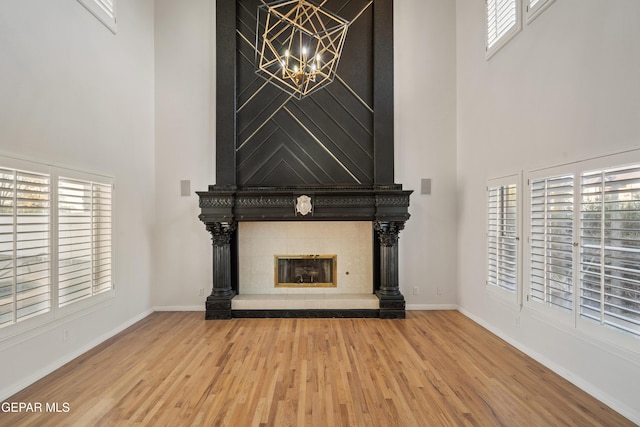 unfurnished living room with a fireplace, a wealth of natural light, a towering ceiling, and hardwood / wood-style flooring