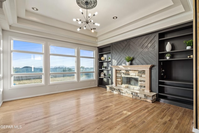 unfurnished living room with hardwood / wood-style flooring, a tray ceiling, a fireplace, a chandelier, and built in shelves