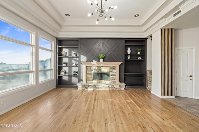 unfurnished living room with a stone fireplace, built in features, a chandelier, hardwood / wood-style flooring, and a tray ceiling