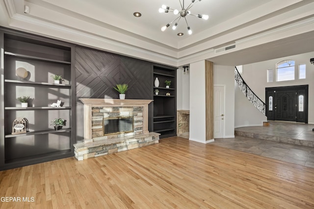 unfurnished living room featuring built in shelves, wood-type flooring, a fireplace, and a chandelier