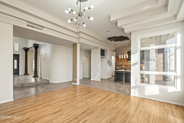 unfurnished living room featuring a raised ceiling, a notable chandelier, light hardwood / wood-style floors, and ornate columns