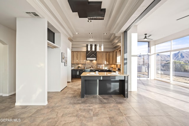 kitchen featuring a mountain view, ceiling fan, tasteful backsplash, decorative light fixtures, and light stone counters