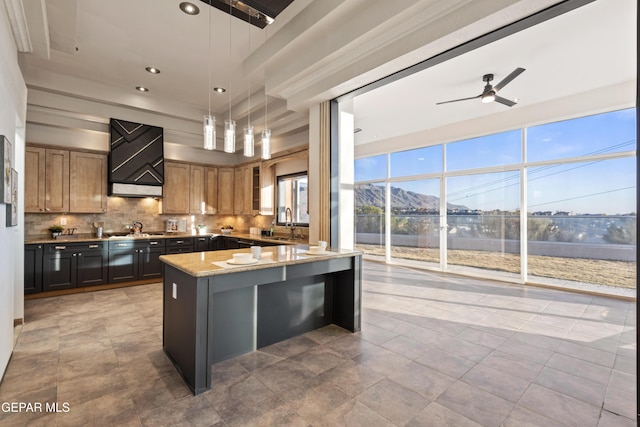 kitchen with pendant lighting, a kitchen island, tasteful backsplash, ceiling fan, and light stone counters