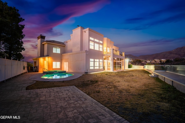 back house at dusk with a mountain view, a patio area, a balcony, and a fenced in pool