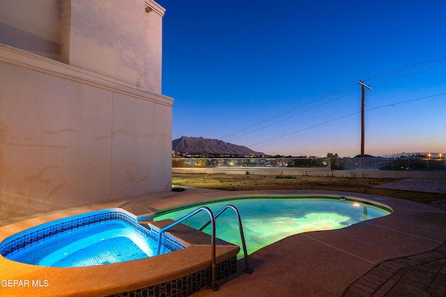 pool at dusk with a patio area, a mountain view, and an in ground hot tub