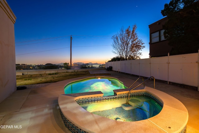 pool at dusk featuring an in ground hot tub and a patio