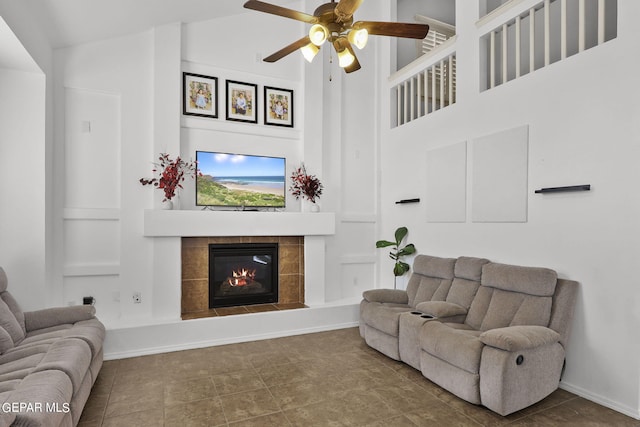 living room featuring ceiling fan, a towering ceiling, and a tiled fireplace