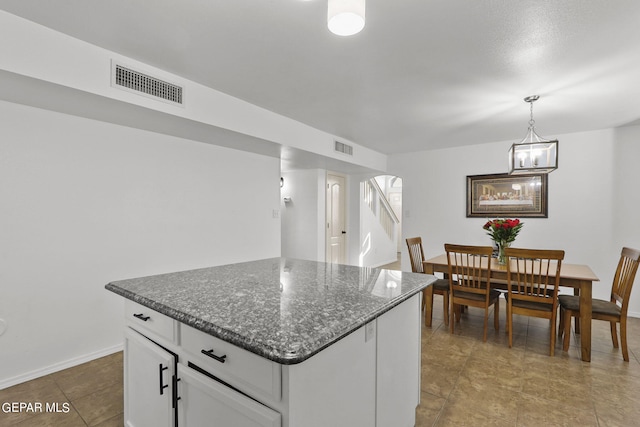 kitchen with white cabinets, a center island, dark stone counters, an inviting chandelier, and hanging light fixtures