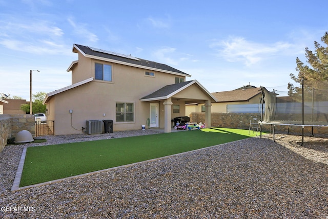 rear view of house with central air condition unit, a trampoline, a patio area, solar panels, and a yard