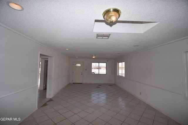 empty room featuring a textured ceiling, a skylight, light tile patterned floors, and ornamental molding