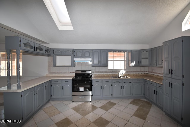 kitchen featuring gray cabinets, vaulted ceiling with skylight, stainless steel gas stove, and sink