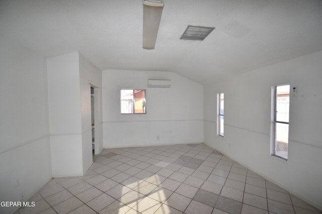 empty room with lofted ceiling, light tile patterned floors, a textured ceiling, and a wall mounted air conditioner