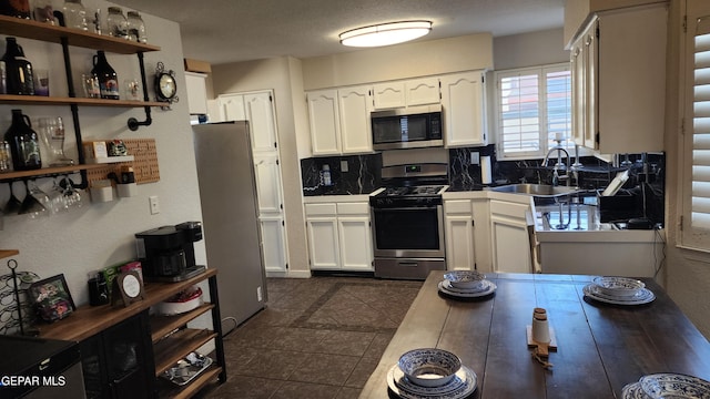 kitchen featuring backsplash, sink, dark tile patterned floors, stainless steel appliances, and white cabinets