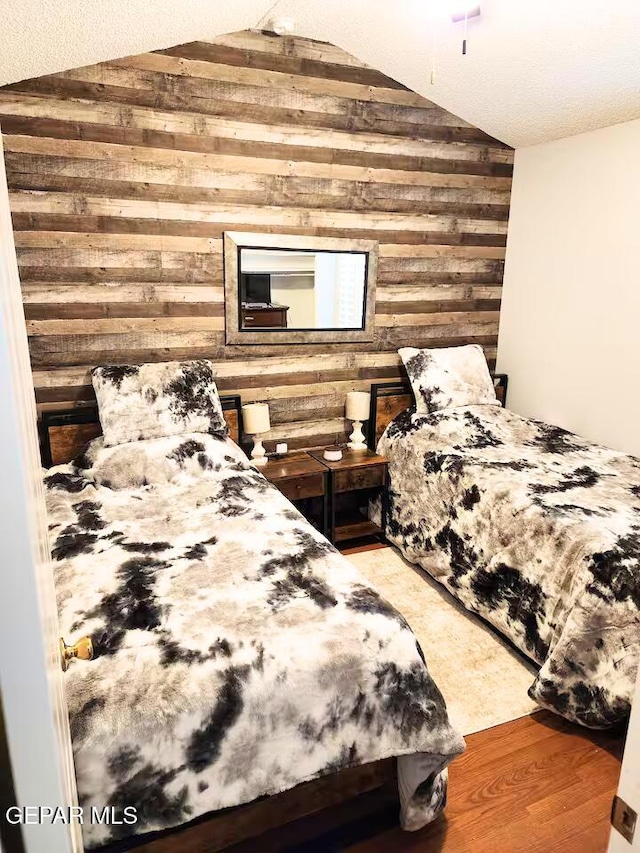 bedroom featuring hardwood / wood-style floors, wood walls, and vaulted ceiling