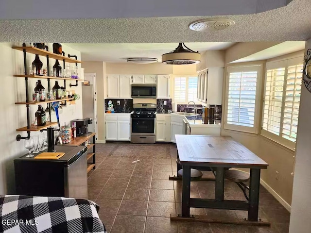 kitchen featuring appliances with stainless steel finishes, dark tile patterned flooring, white cabinetry, and sink