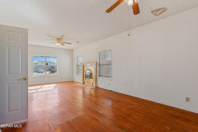 unfurnished living room with ceiling fan, a tile fireplace, light hardwood / wood-style flooring, and a textured ceiling