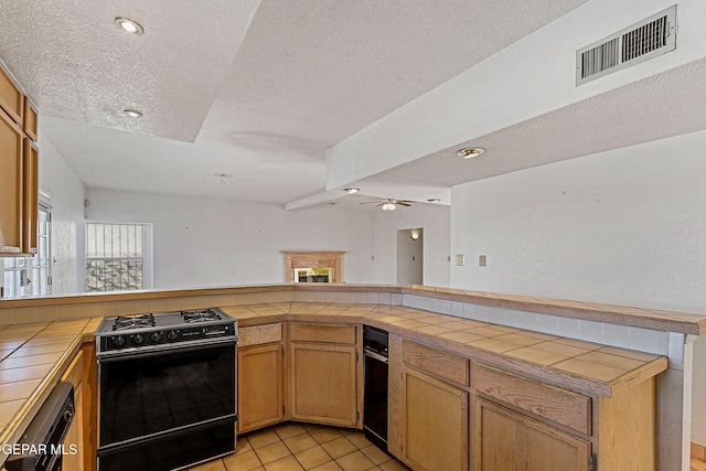 kitchen featuring ceiling fan, kitchen peninsula, light tile patterned flooring, tile counters, and gas range