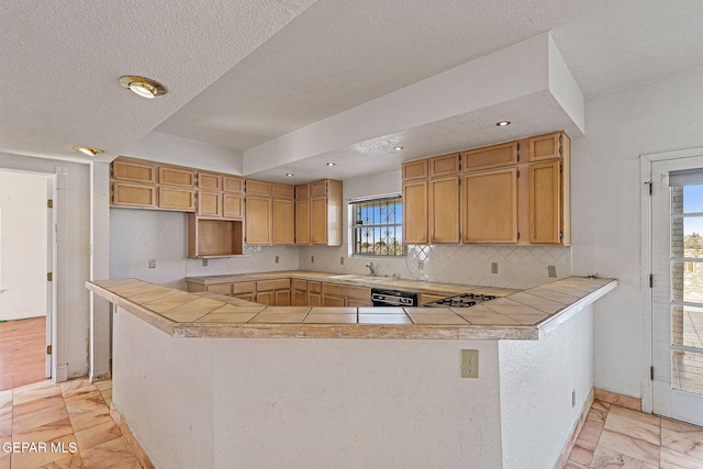 kitchen featuring tile countertops, kitchen peninsula, backsplash, dishwasher, and sink