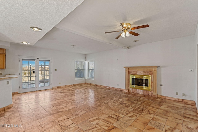 unfurnished living room featuring a textured ceiling, beamed ceiling, french doors, ceiling fan, and a tile fireplace