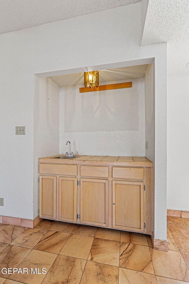 bar with a textured ceiling, light brown cabinetry, and sink