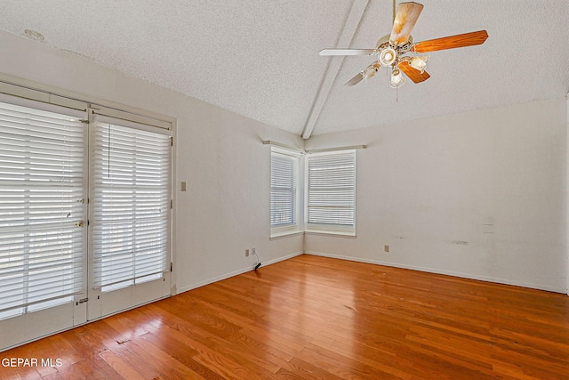 spare room with ceiling fan, vaulted ceiling with beams, a textured ceiling, and hardwood / wood-style floors