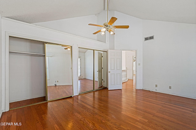 unfurnished bedroom with ceiling fan, high vaulted ceiling, hardwood / wood-style flooring, and two closets