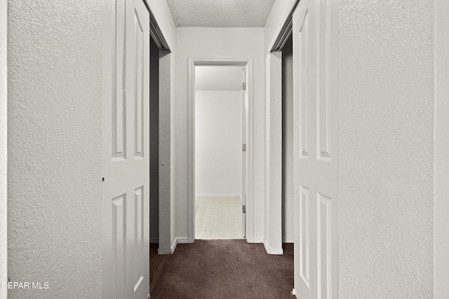 corridor with a textured ceiling and dark carpet