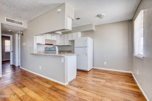 kitchen featuring a textured ceiling, white cabinetry, white refrigerator, light hardwood / wood-style floors, and kitchen peninsula