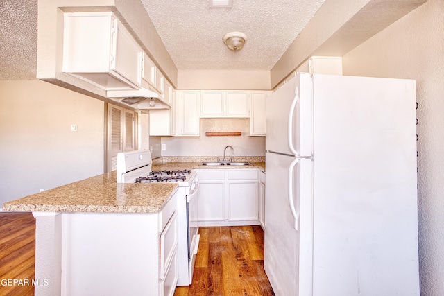 kitchen featuring white appliances, hardwood / wood-style floors, white cabinetry, sink, and kitchen peninsula