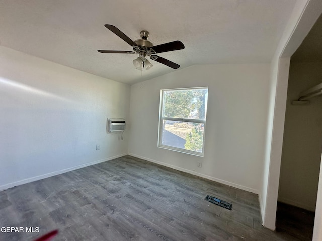 unfurnished bedroom featuring ceiling fan, vaulted ceiling, hardwood / wood-style flooring, and a wall mounted air conditioner