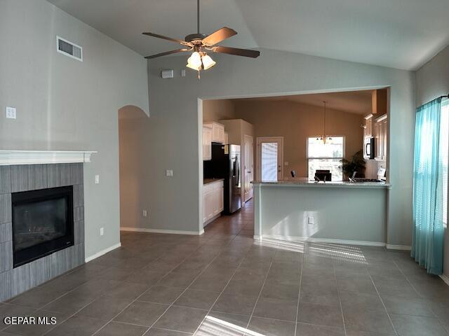 unfurnished living room featuring ceiling fan, dark tile patterned floors, a tile fireplace, and vaulted ceiling