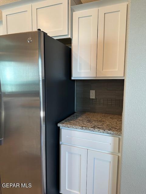 kitchen with tasteful backsplash, stainless steel refrigerator, light stone counters, and white cabinetry