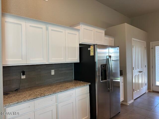 kitchen with dark tile patterned flooring, decorative backsplash, light stone countertops, stainless steel fridge with ice dispenser, and white cabinets