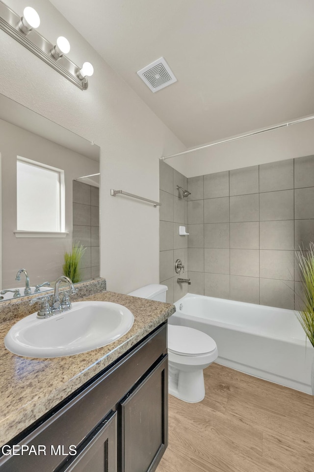 full bathroom with wood-type flooring, toilet, tiled shower / bath combo, and vanity