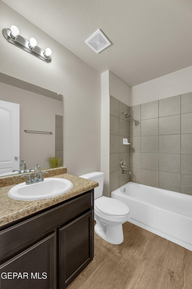 full bathroom with toilet, hardwood / wood-style floors, a textured ceiling, and tiled shower / bath combo