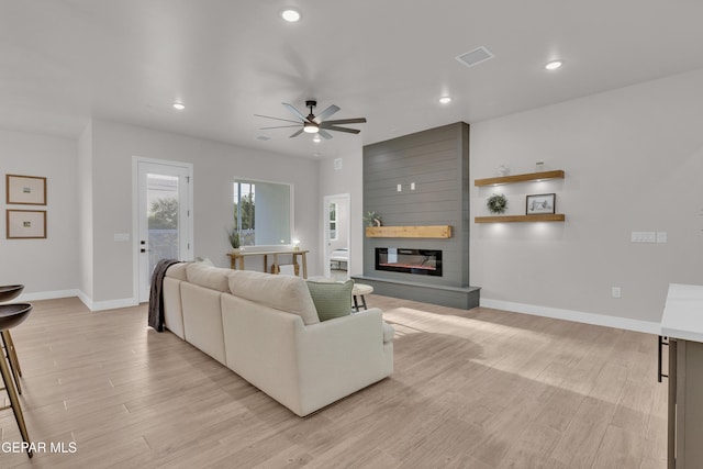 living room featuring ceiling fan, a large fireplace, and light wood-type flooring