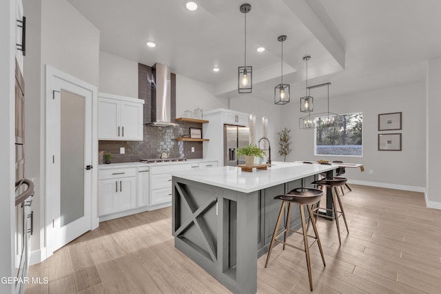 kitchen featuring wall chimney exhaust hood, appliances with stainless steel finishes, a center island with sink, and white cabinets