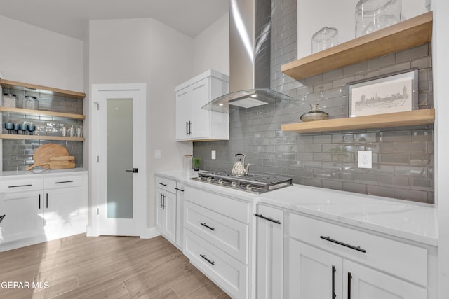 kitchen featuring wall chimney exhaust hood, stainless steel gas cooktop, light stone counters, decorative backsplash, and white cabinets