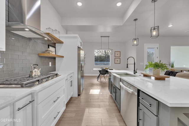 kitchen with white cabinetry, wall chimney range hood, light stone counters, and appliances with stainless steel finishes