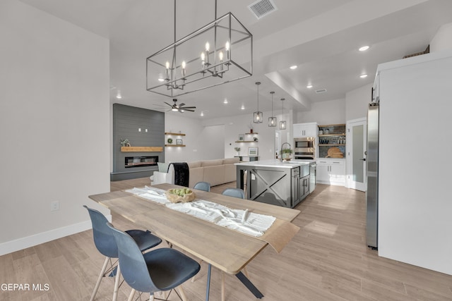 dining area with ceiling fan, sink, a large fireplace, and light hardwood / wood-style floors