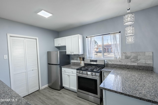 kitchen featuring stainless steel appliances, backsplash, light wood-style flooring, white cabinets, and dark stone countertops