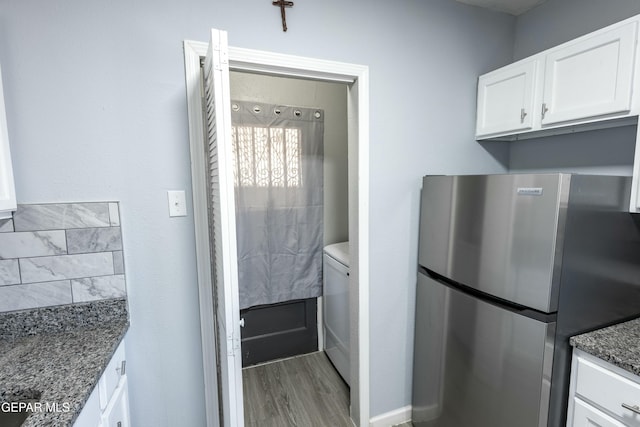 kitchen with hardwood / wood-style floors, white cabinets, dark stone counters, and stainless steel refrigerator